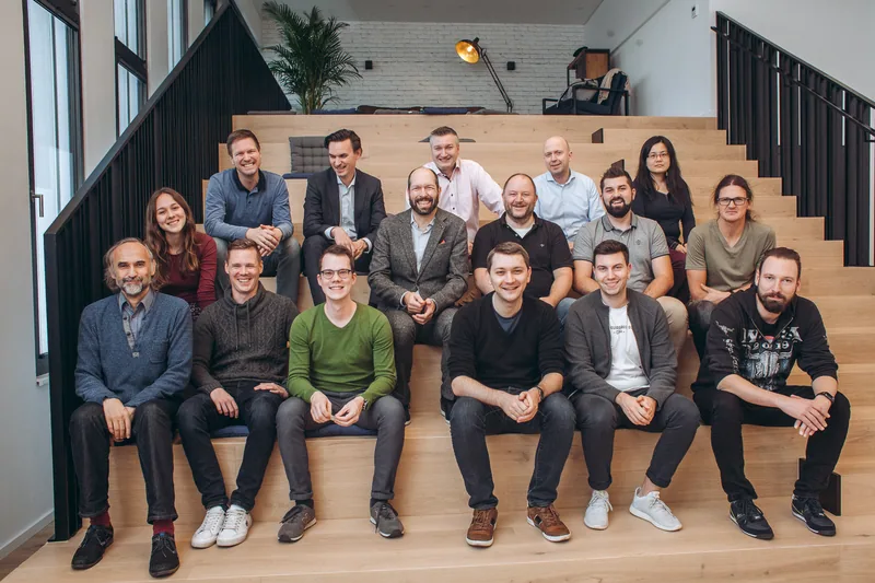 Ein Team von rund einem Dutzend Menschen sitzt für ein Gruppenfoto auf einer hölzernen Sitztreppe.