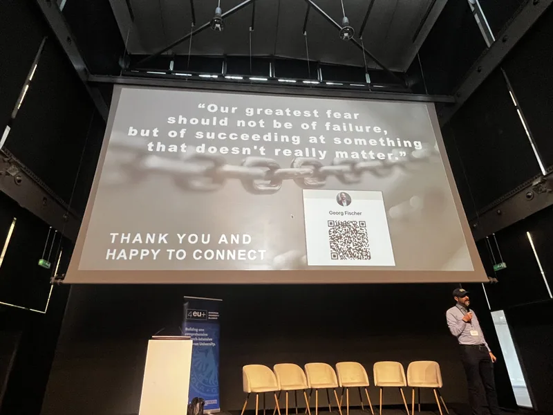 Georg Fischer steht klein am rechten Rand einer abgedunkelten Bühne; die Großleinwand über ihm zeigt den Satz Our greatest fear should not be of failure, but of succeeding at something that doesn't really matter.