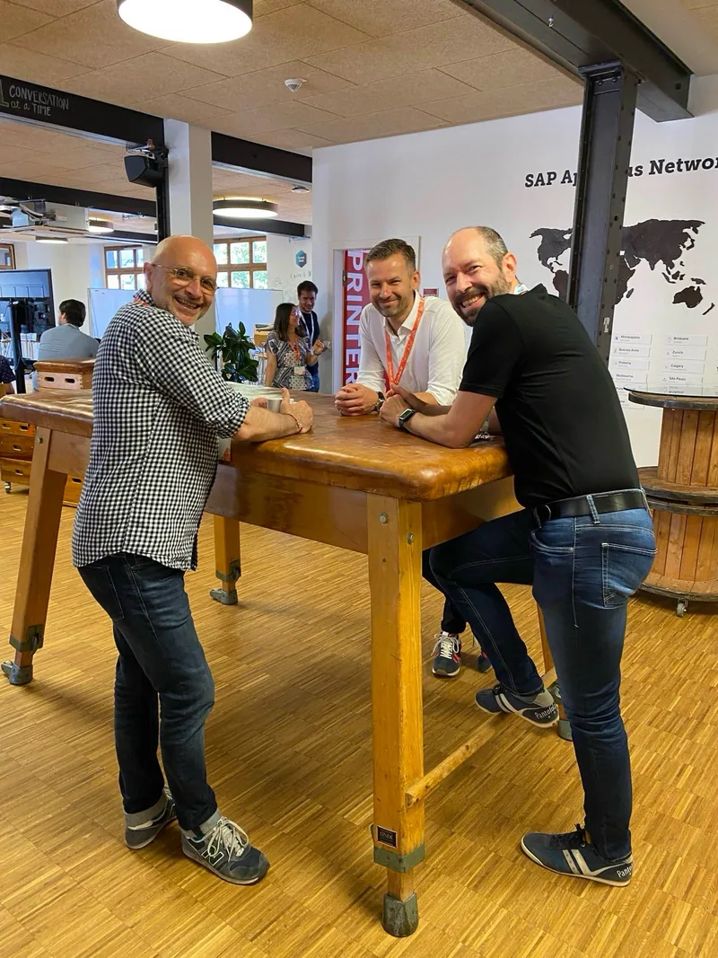 Zwei Personen lachen gemeinsam an einem Holztisch in einem Coworking-Raum.