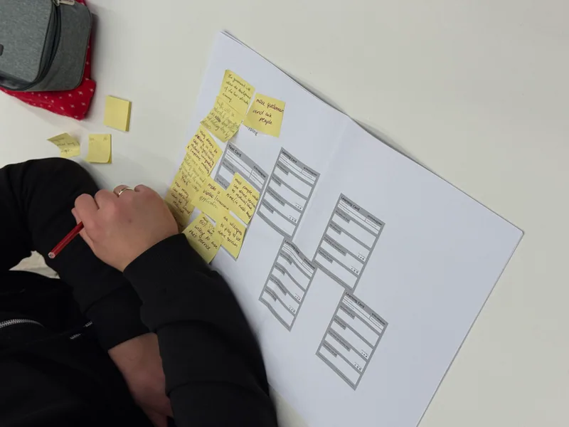 Eine Person schreibt zwischen gelben Notizzetteln auf einem ausgedruckten Learning-Card-Bogen.