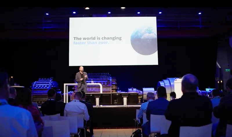 Ein verdunkelter Saal mit großer Projektion "The world is changing faster than ever", davor der Redner und das Publikum.