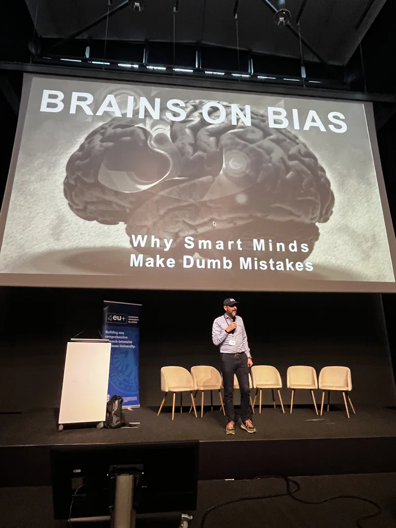 Der Redner steht mittig auf der Bühne vor der Projektion "Brains on Bias".